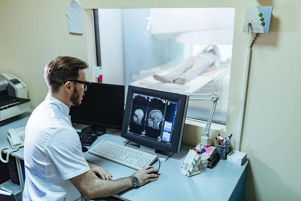 Doctor supervising brain scan procedure of a patient from control room